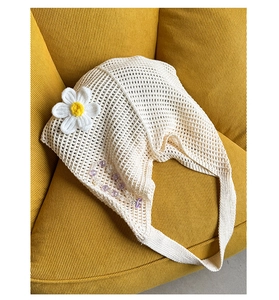 Detail der beigen Häkeltasche mit gestrickter Gänseblümchenblüte und lila Perlenkette