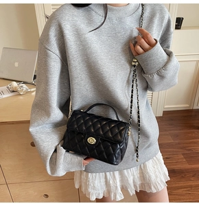 Detail of black quilted crossbody bag featuring a gold twist lock and leather chain strap