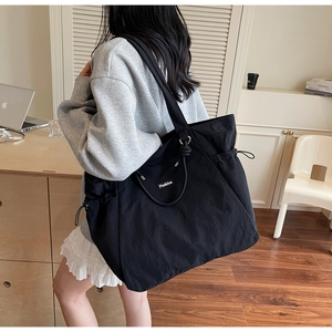 Detail of a large black nylon tote bag with drawstring sides and Fashion label