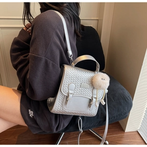 Détail d'un sac à dos argenté avec rabat tissé et pompon blanc porté par un modèle