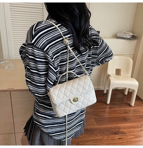 Detailed view of white quilted square bag with gold metal chain strap and spherical buckle