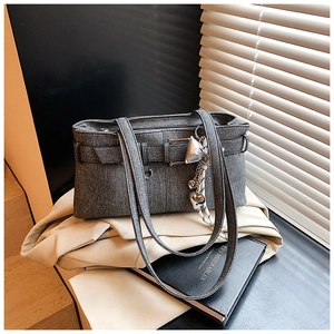 Detail of dark grey bucket bag with silver bow charm on soft off-white blazer