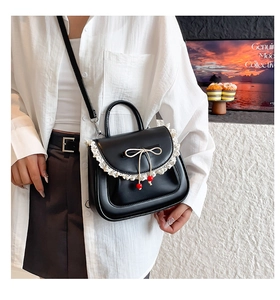 Dettaglio della borsa in pelle PU nera con pizzo bianco e fiocco beige con ciondoli ciliegia