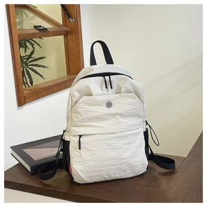 Detail of cream-white backpack with textured fabric and metal logo on a wooden table