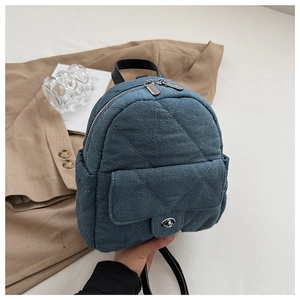 Close-up of blue denim quilted backpack featuring a silver twist lock and dual zippers