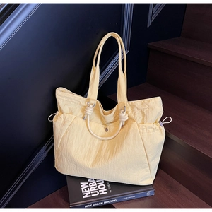 Detail of light yellow nylon tote bag featuring knot handles and drawstring closure on stairs
