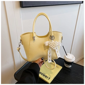 Detail of yellow pleated leather bucket bag with pearl heart and lace bow accessories