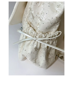 Détail du tissu jacquard argenté avec strass et nœud décoratif en cuir blanc