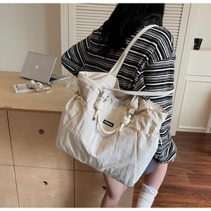 Close-up of beige nylon tote bag with knot handle detail and Fashion label