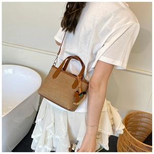 Detail of a brown woven canvas handbag with a horse charm accessory and leather strap