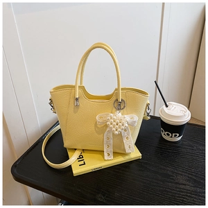 Detail of yellow bucket bag with pleat texture and pearl butterfly charm on desk