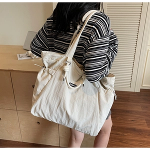 Detailed side view of a large cream nylon tote bag with drawstring side and fashion label