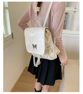 Detailed view of silver butterfly charms and ribbon drawstring on the white backpack