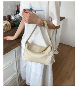 Detail of cream shoulder bag featuring pebbled texture and pearl lace bow accessory