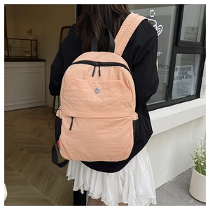 Detail view of pink nylon backpack featuring metal logo and adjustable black straps