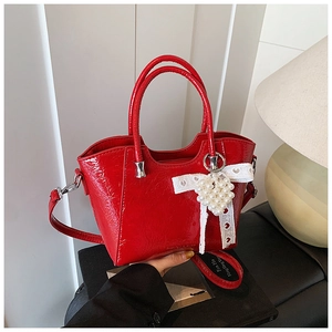 Close-up of a bright red patent leather bucket bag with a white lace pearl heart charm