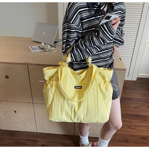 Detail of yellow nylon tote bag featuring side drawstrings and a black Fashion label tag