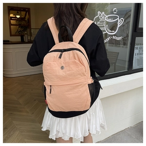 Pale pink nylon backpack with black zipper accents worn by a model in a cafe setting