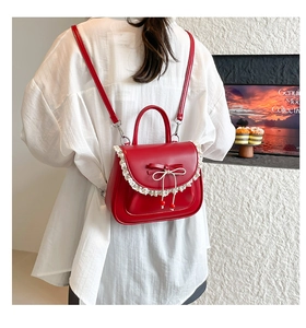 Dettaglio dello zaino in pelle rossa con bordo in pizzo bianco e decorazione con fiocco