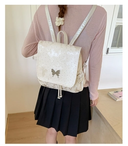 Close-up of butterfly embroidery detail and silver metal buckle on a cream backpack
