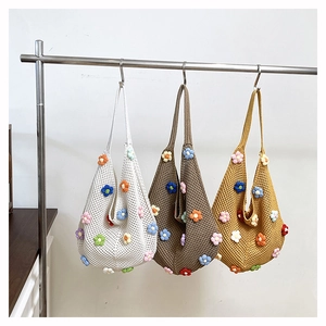 Three colorful handmade crochet tote bags with floral patterns hanging on a metal rack
