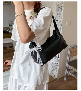 Detail of black pebbled leather handbag featuring white lace bow and pearl tassel accents