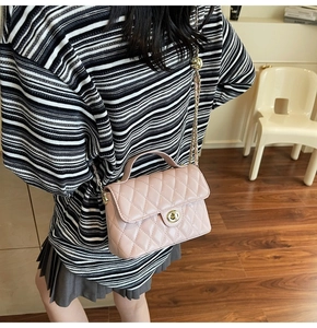 Detail view of pink quilted handbag with gold clasp and chain strap worn by model