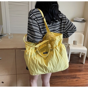 Detail of a bright yellow nylon tote bag with drawstring sides and Fashion label