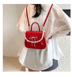 Dettaglio dello zaino in pelle rossa con pizzo bianco e ciondoli a fiocco eleganti
