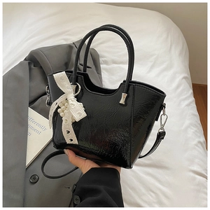 Detail of glossy black bucket bag with pleated texture and lace pearl bow charm