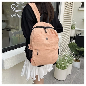 Outdoor view of a salmon pink nylon backpack with black zipper accents and metal logo