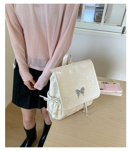 Détail du sac à dos blanc crème avec ornement papillon argenté et poche latérale à cordon