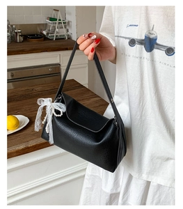 Close-up of black leather dumpling bag with white lace bow and pearl charm detailing