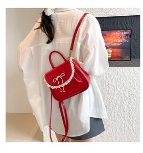Dettaglio dello zaino rosso con fiocco e pizzo indossato su una camicia bianca moda