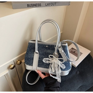 Detail der blauen Denim-Tasche mit silbernem Lederbesatz und weißem Spitzenbogen-Anhänger