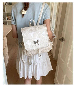 Detail of butterfly metal buckle and soft print on a cream-colored fashion backpack