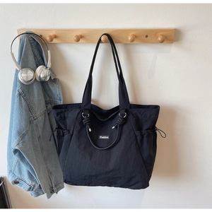 Detail of black nylon tote bag featuring functional side drawstring and Fashion cloth label
