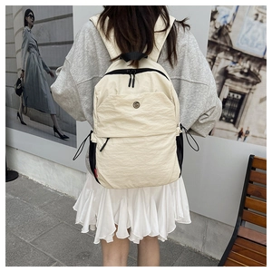 Detail view of cream nylon backpack featuring black zippers and metal logo on the front pocket