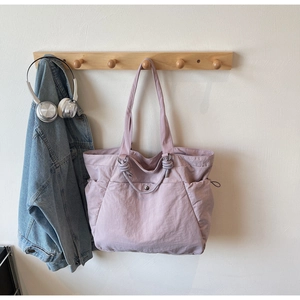 Detail view of a lavender nylon tote bag with drawstring side pockets on a wall hook