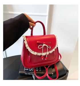 Dettaglio dello zaino rosso con fiocco e pizzo bianco, mostrato con un libro di moda