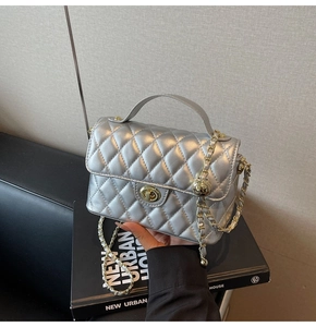 Detail of silver quilted crossbody bag with gold twist lock and chain strap on a book