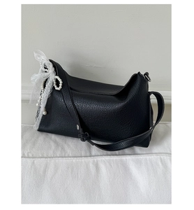 Close-up of black lychee leather handbag with white lace bow and pearl charm detail