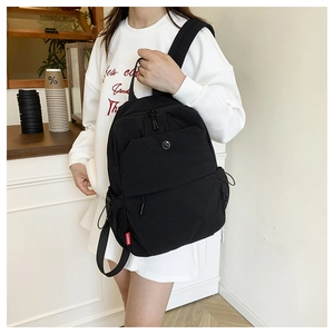 Detail of a casual black nylon backpack featuring a distinctive red woven side label and logo