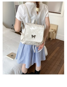 Detail of white butterfly embossed backpack with metallic butterfly buckle and embroidery