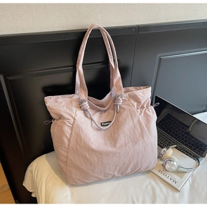 Large pale pink nylon tote bag with side drawstrings and Fashion label on white bedding