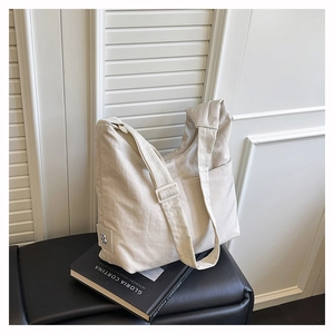 Minimalist beige half-moon nylon tote bag with adjustable strap on a leather bench