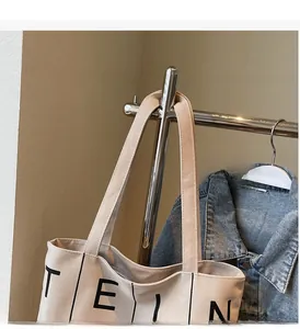 Detailed close-up of beige canvas tote bag with black lettering and sturdy handles