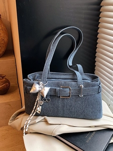Blue denim texture bucket bag with silver buckle and heart charm on a beige blazer