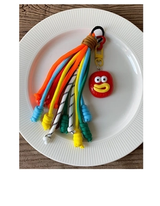 Detail of colorful woven paracord charm with a playful cartoon face and red heart clip