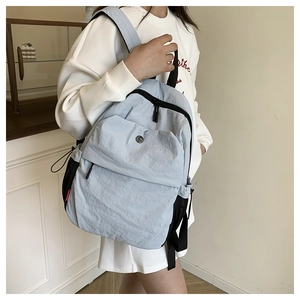 Detail view of a light blue nylon backpack with multiple pockets shown on model